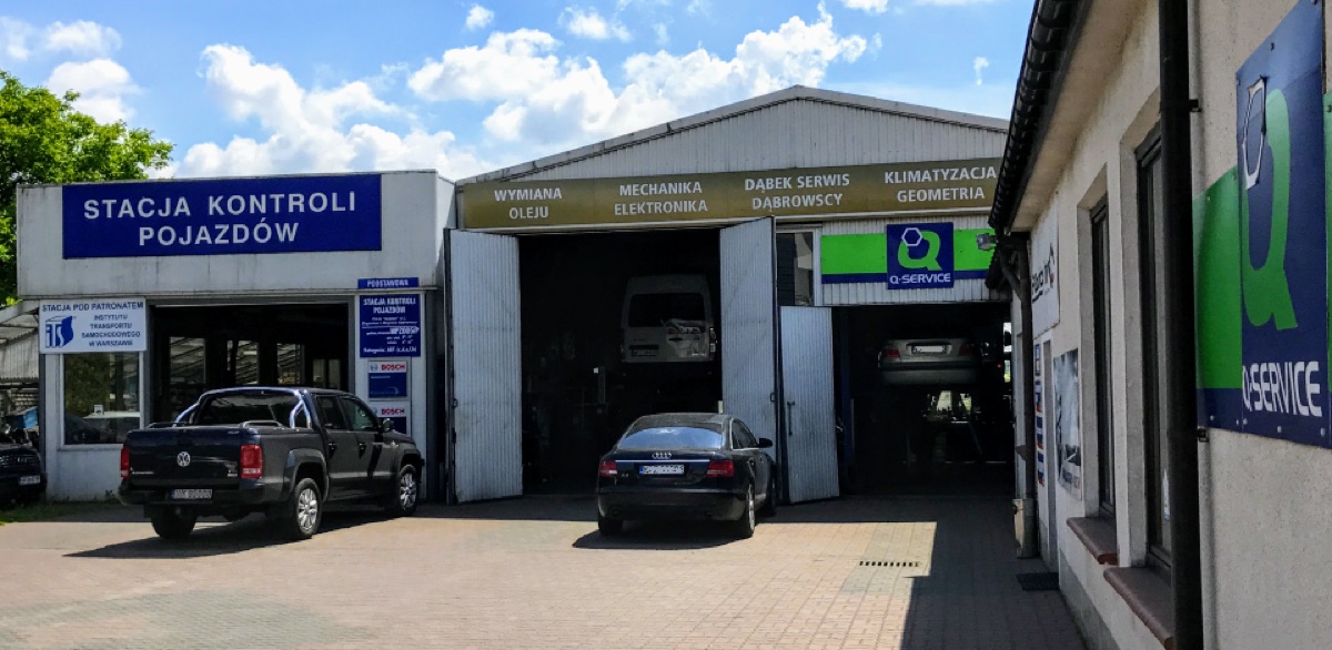 Serwis samochodowy Dąbek w Przasnyszu: budynek stacji kontroli pojazdów, hala serwisowa z napisem „DĄBEK SERWIS” nad otwartą bramą, samochody na podnośnikach i szyld Q Service